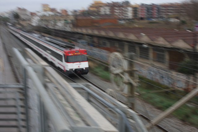A red and white commuter train blurring past graffitied trackside sheds