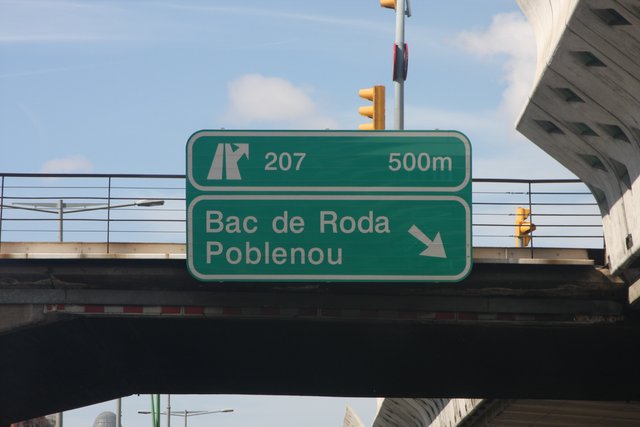 Green motorway exit sign for Bac de Roda and Poblenou beneath a concrete overpass
