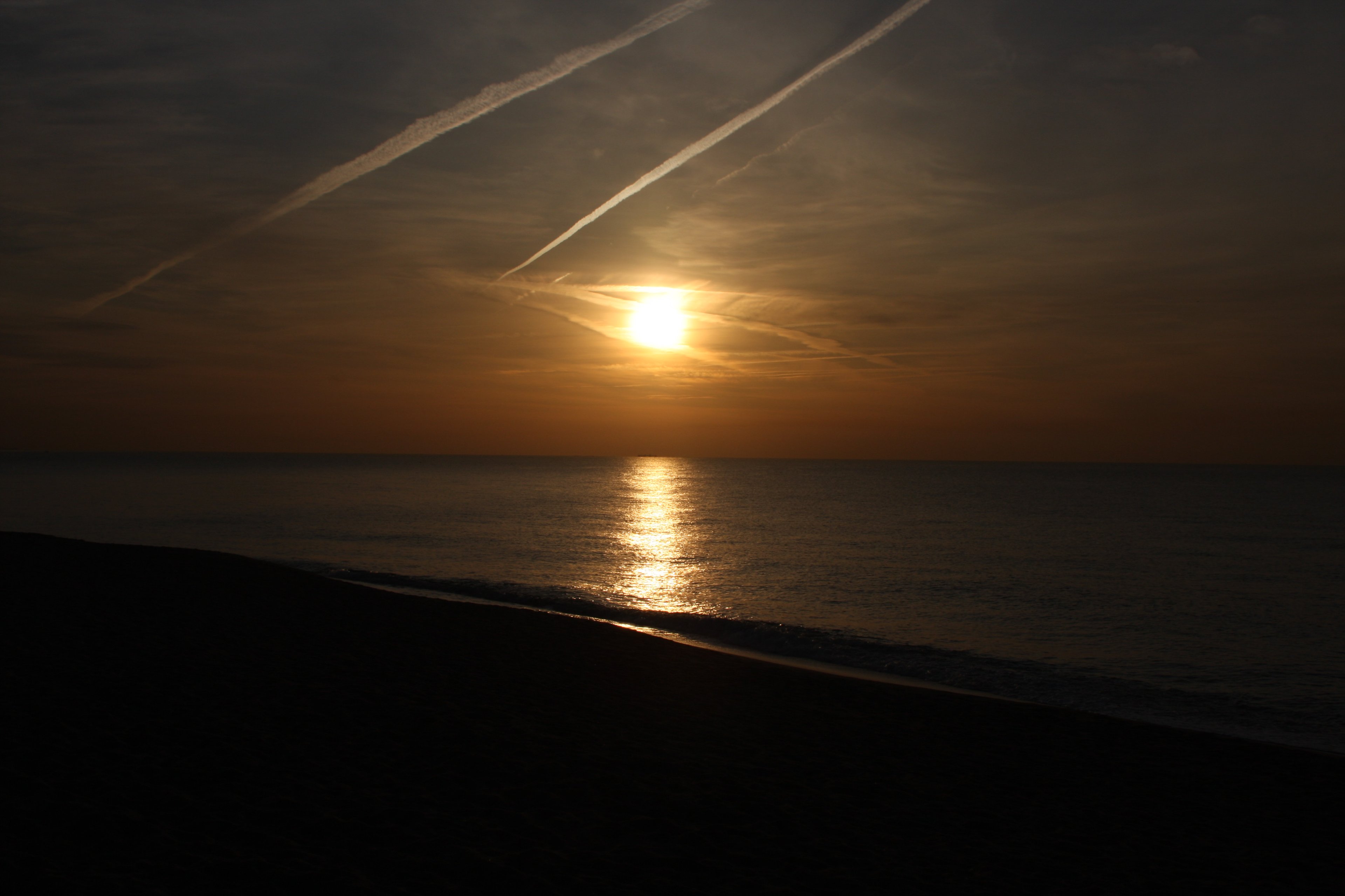 Low sun over a dark sea, contrails crossing the sky above