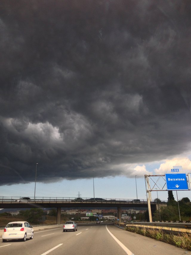 Storm cloud spreading over a motorway beneath a blue sign for Barcelona