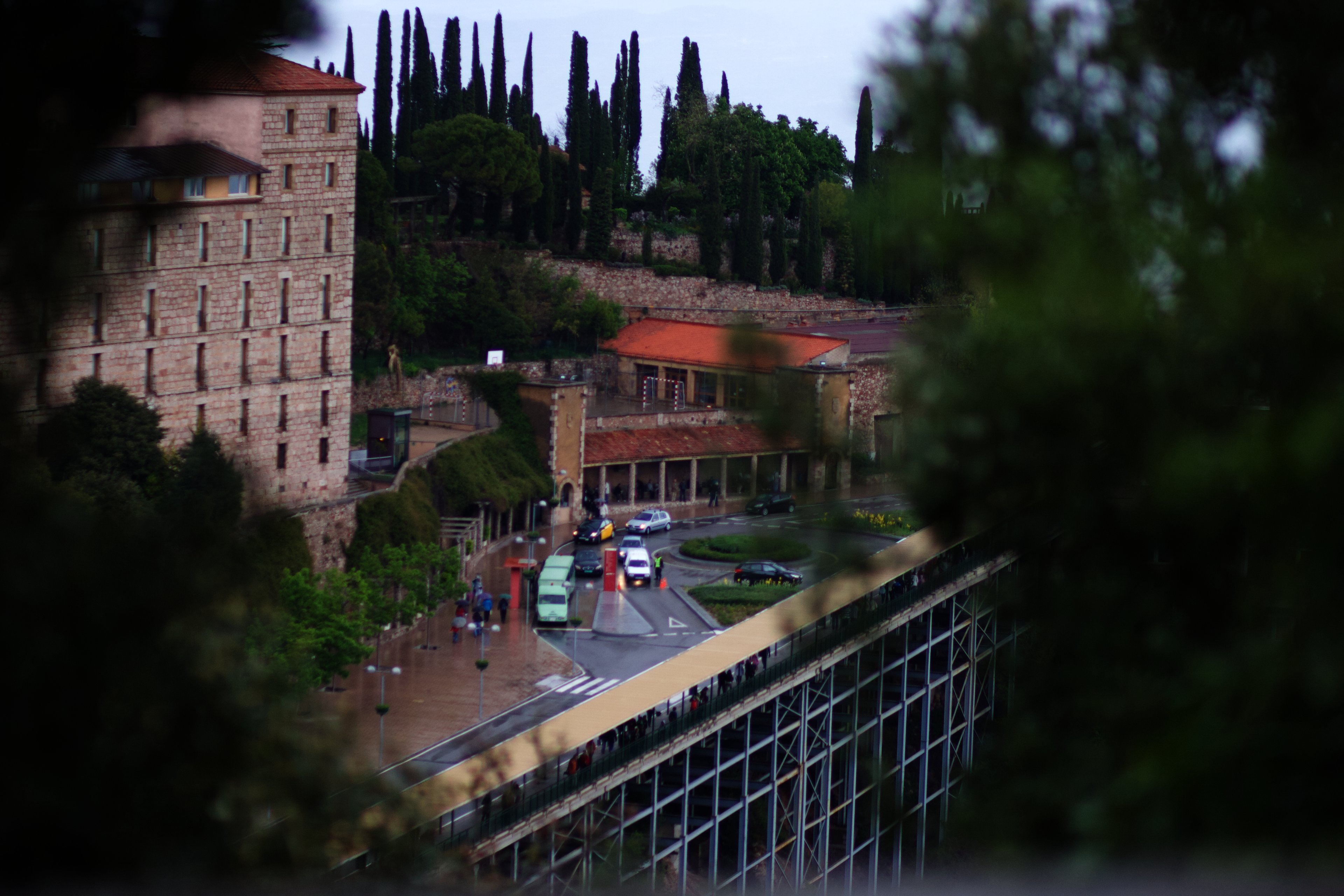 Montserrat monastery buildings among cypress trees, seen through foliage on a wet day