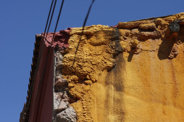 Crumbling ochre and pink wall corner under overhead wires against blue sky